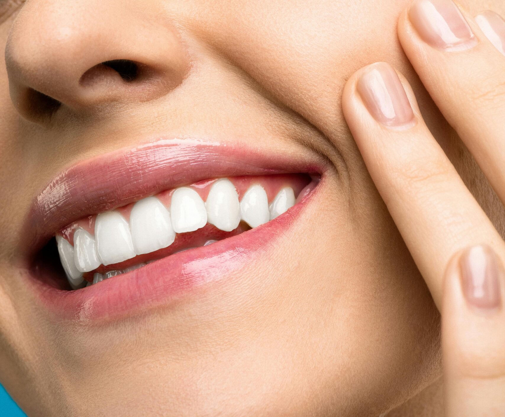 A close-up portrait of a joyful woman with closed eyes, pink lipstick, and her hand touching her cheek.